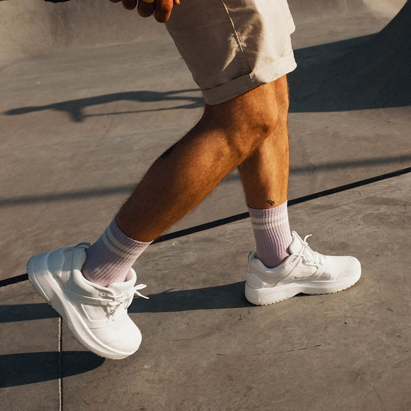 Hvid sporty sneaker på en herrefod med shorts, gående på et hårdt underlag.